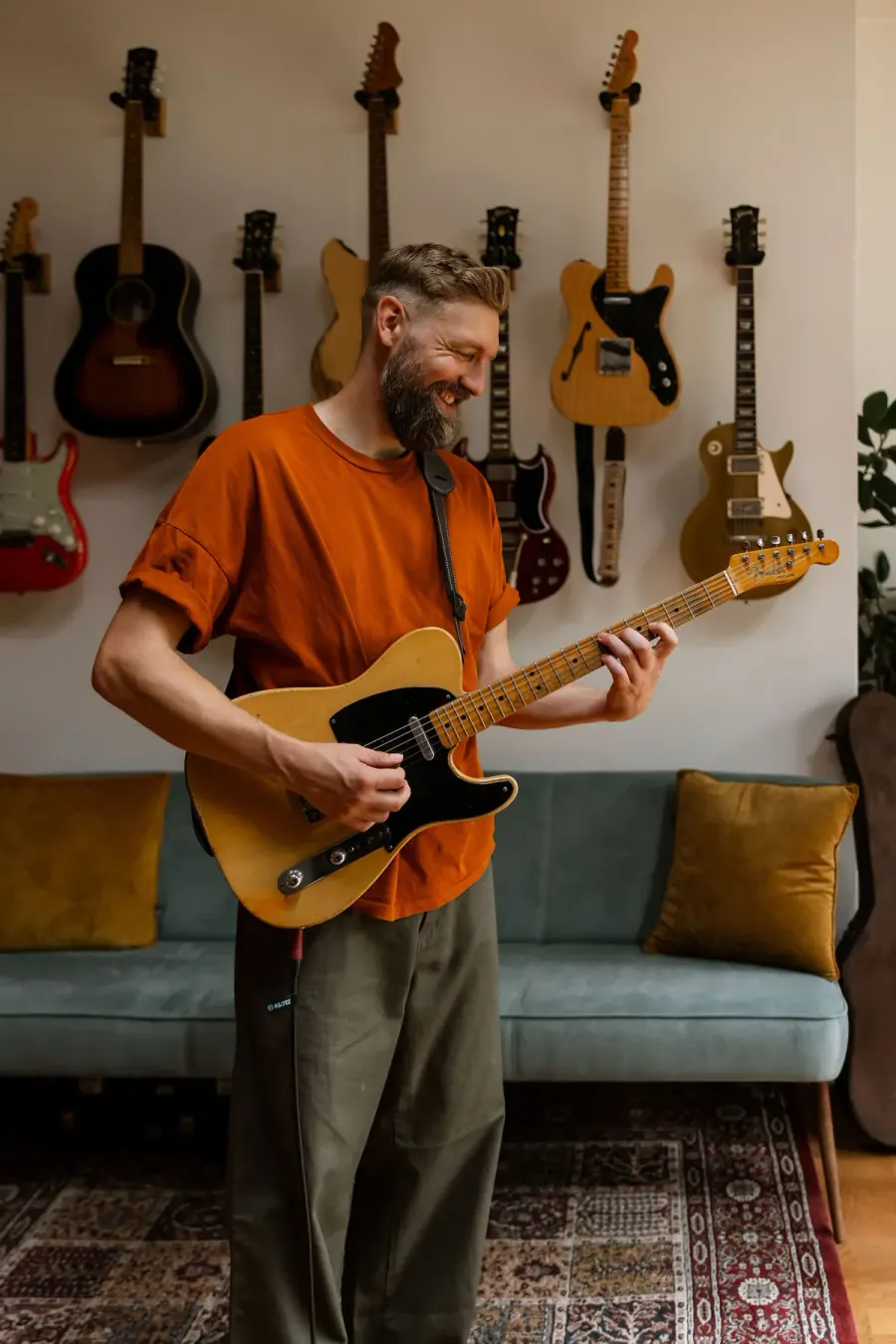 Paul Davids playing a Telecaster in front of a wall of guitars, smiling.