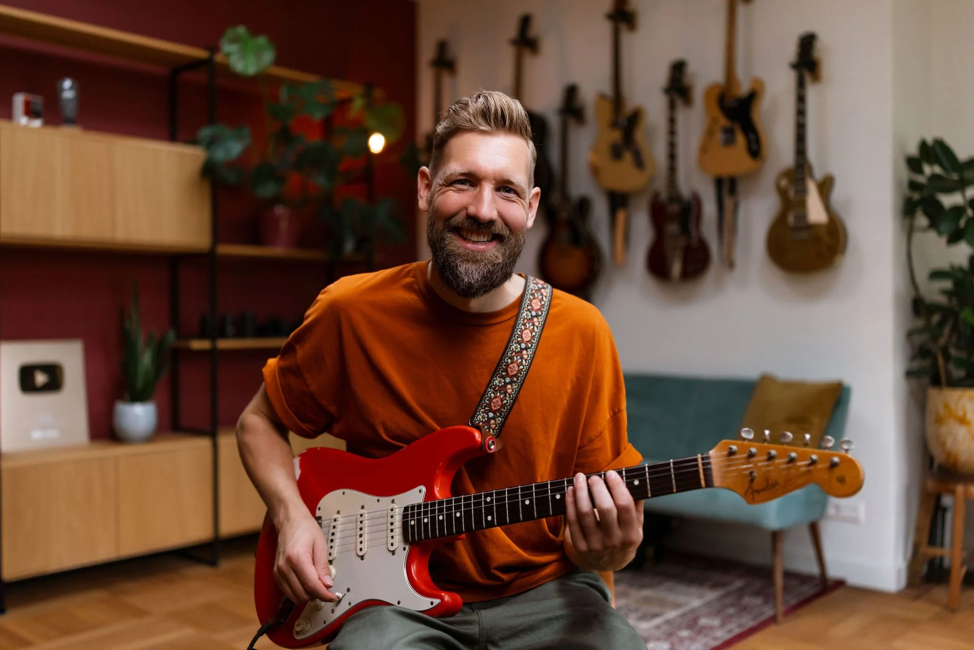 Paul Davids smiling, playing a red Stratocaster in his studio